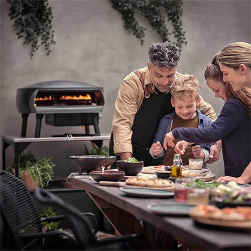 Familie am Outdoor-Tisch mit Pizzaofen und Speisen auf der Terrasse